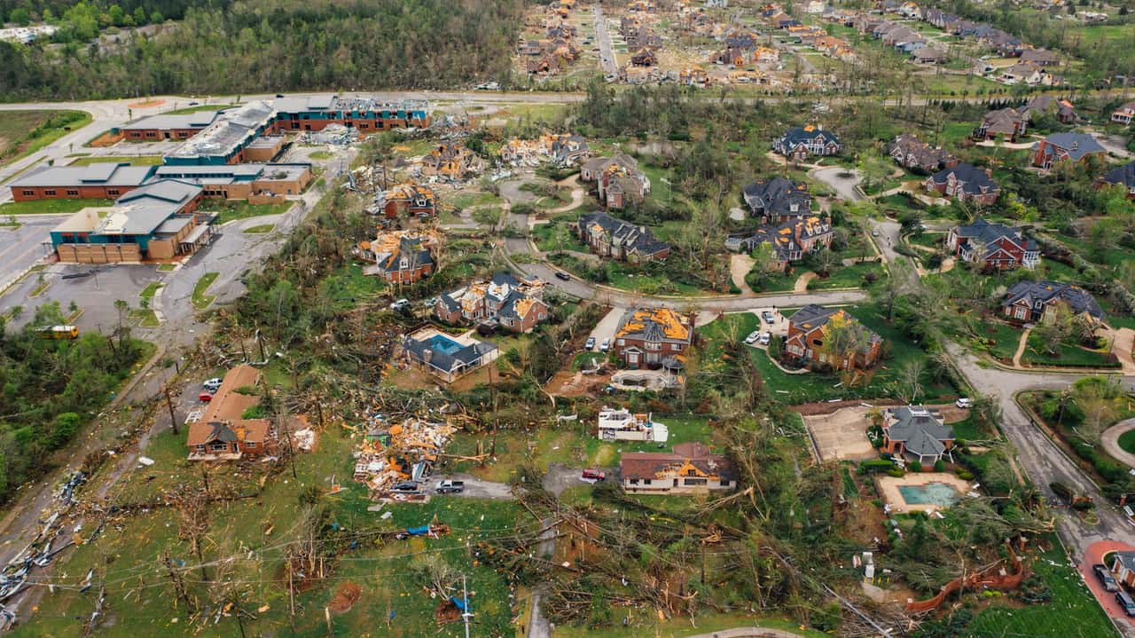 Aerial view of a neighborhood with damaged roofs and downed trees after a severe storm