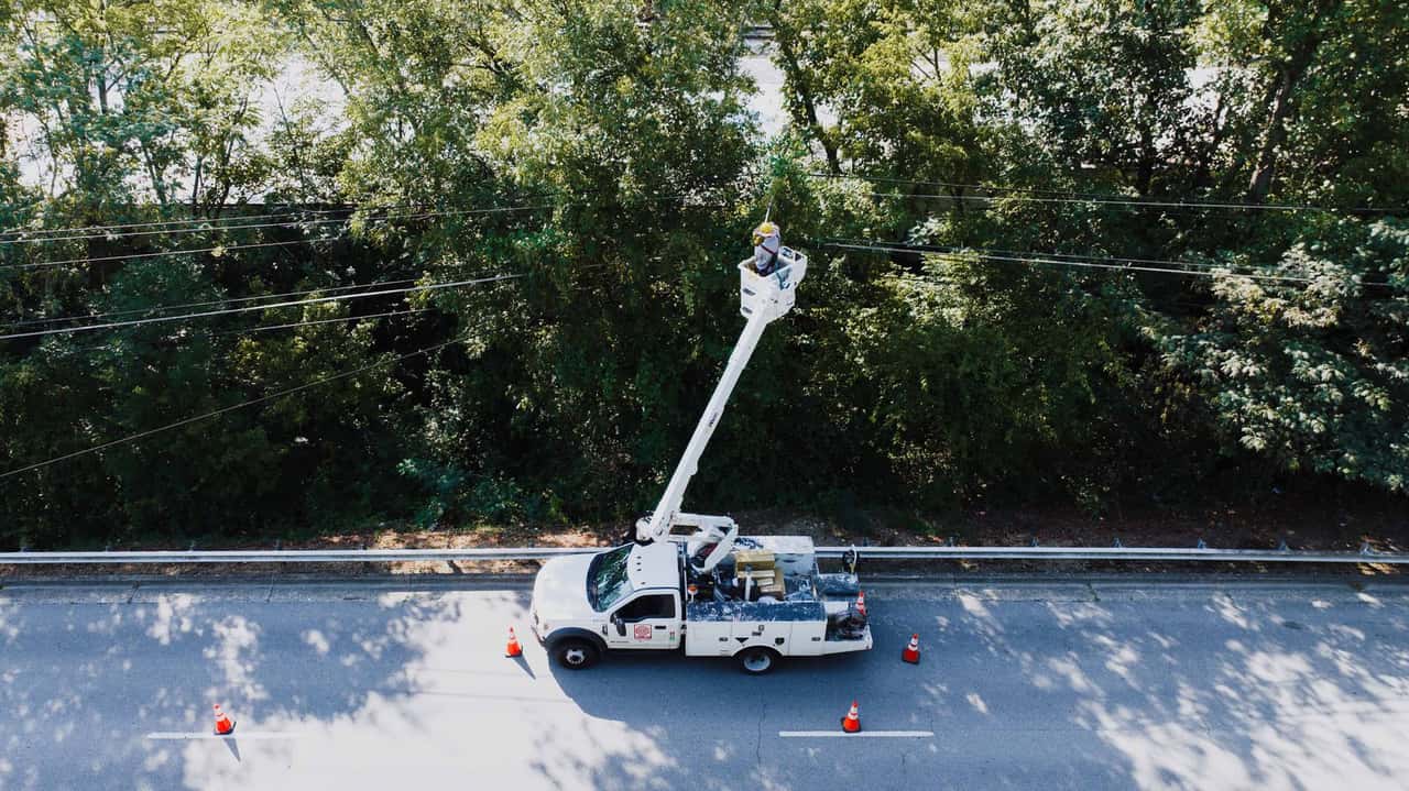 Bucket truck with its boom raised beside trees and overhead lines on a street