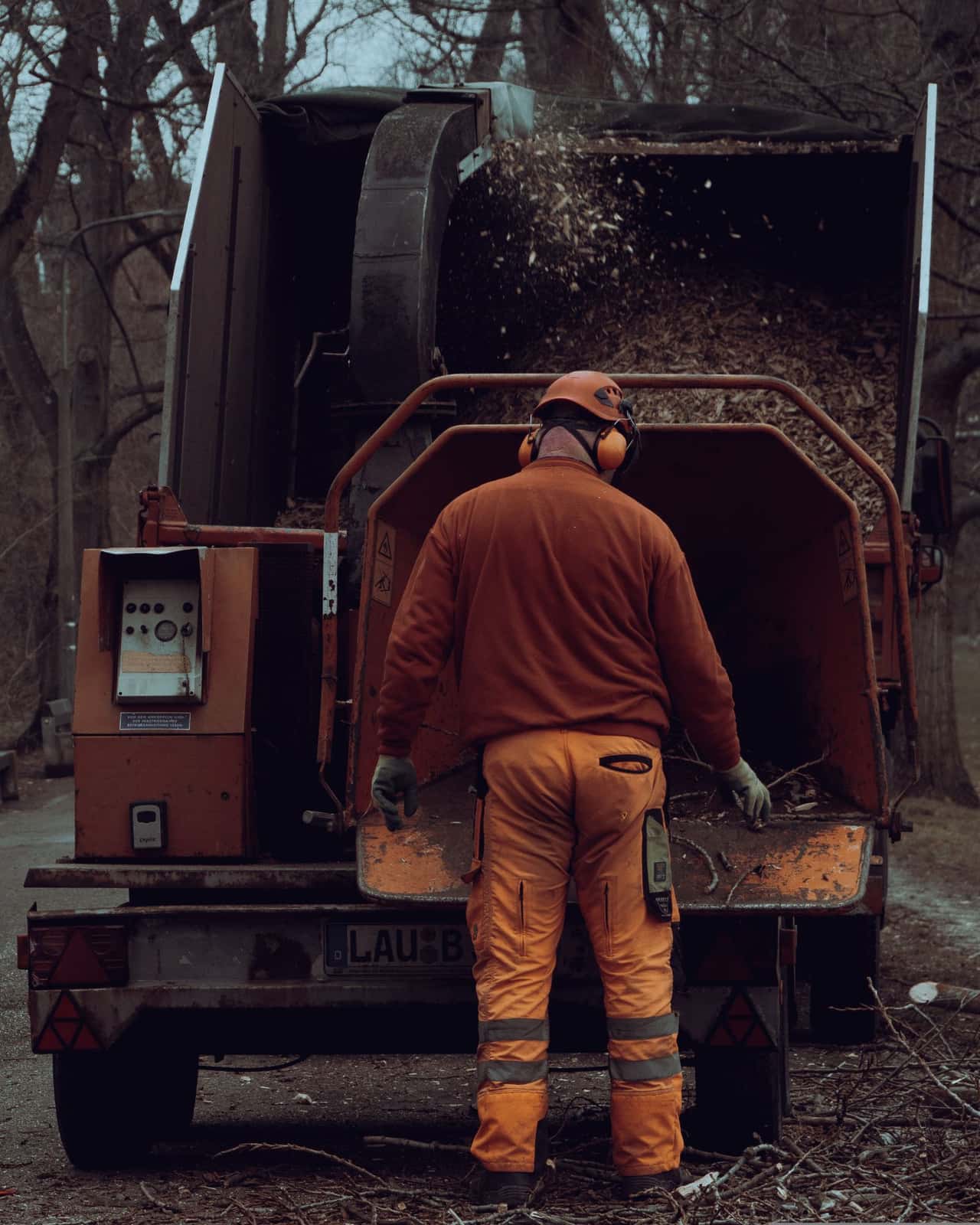 Crew member in hi-vis clothing and ear protection at a wood chipper