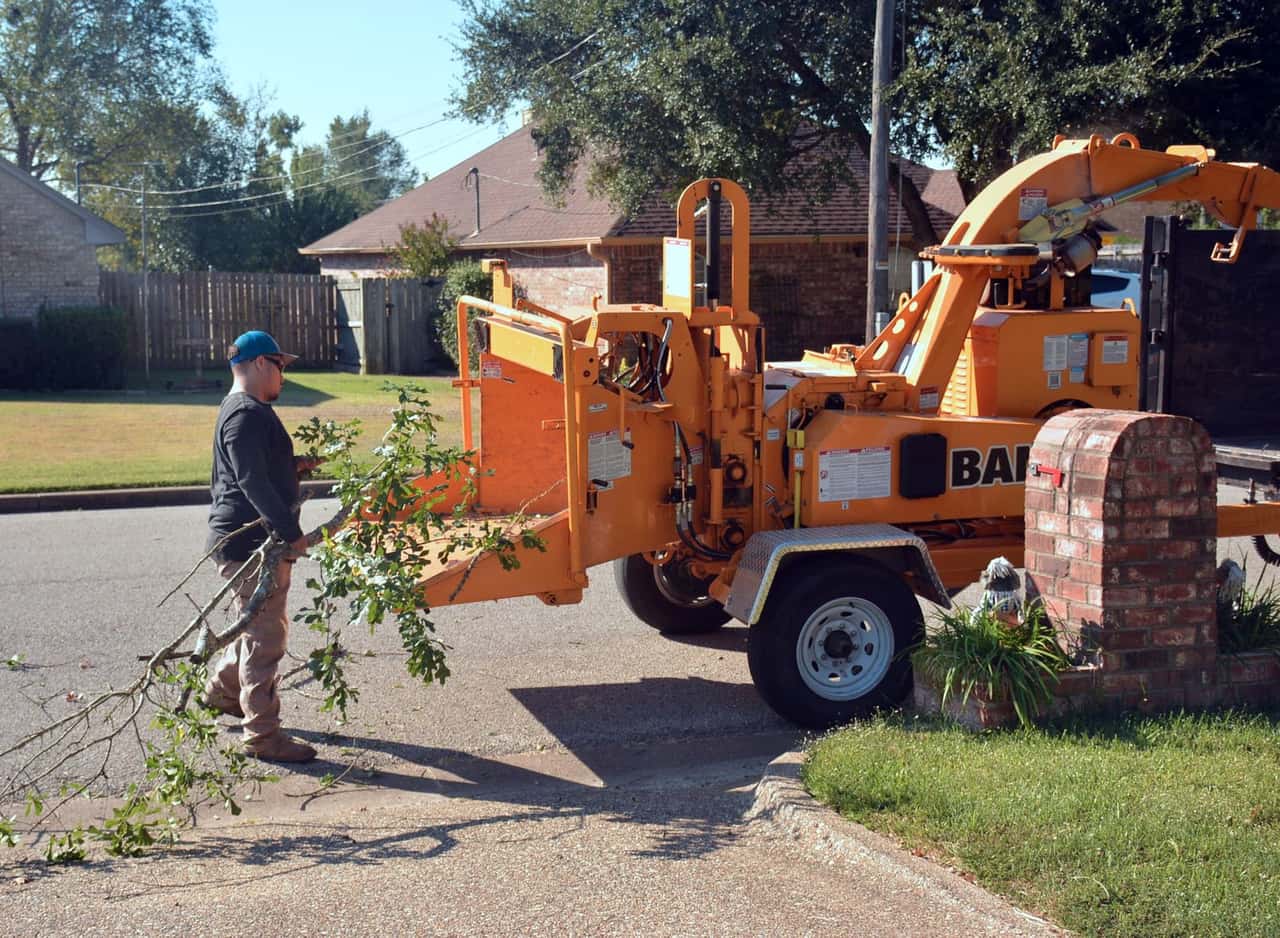 Worker feeding branches into a towable wood chipper on a residential street